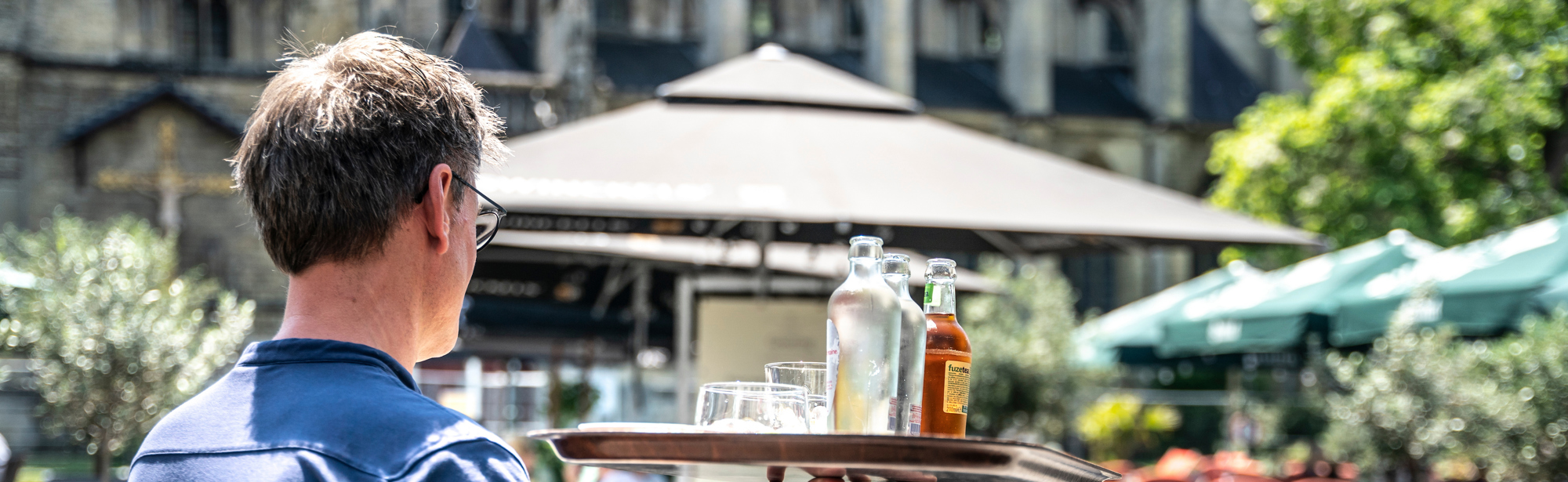 Ober met dienblad met verfrissende drankjes loopt op zomerse dag op Markt in Meerssen